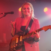 Eivor facing the camera with her eyes closed while holding a guitar.